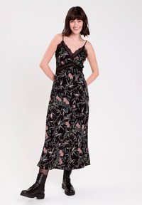 Sort floralt maxi kjole med en v-hals, der har blondekanter, prydet med rosa og grønne botaniske mønstre, og båret med sorte combat støvler.