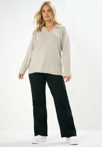 Beige, langärmeliger V-Ausschnitt-Pullover mit strukturiertem Strick; kombiniert mit schwarzen, weit geschnittenen Hosen und weißen Sneakers. Einfaches, lässiges Design.