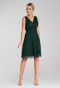 Dunkelgrünes ärmelloses Kleid mit gewickeltem Oberteil und fließendem, knielangem Rock. Hergestellt aus leichtem Stoff mit einem transparenten Überzug.