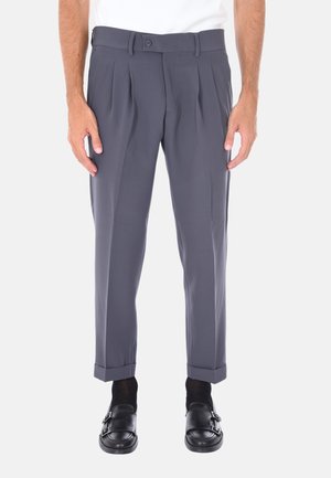 Pantaloni grigi su misura con pieghe, caratterizzati da una texture liscia, design a gamba dritta e orli arrotolati. Indossati con scarpe nere slip-on.