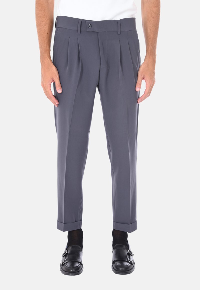 Pantaloni grigi su misura con pieghe, caratterizzati da una texture liscia, design a gamba dritta e orli arrotolati. Indossati con scarpe nere slip-on.