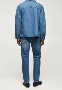 Veste en denim et jeans de couleur bleu moyen. La veste a une coupe légèrement ample avec des coutures visibles et un col standard. Les jeans sont à coupe droite.