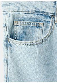 Jean en denim bleu clair avec une petite poche avant à l'intérieur d'une plus grande poche incurvée, détaillée avec des surpiqûres jaunes.