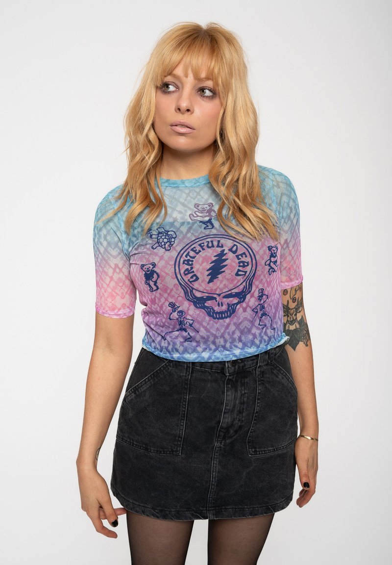 Tie-dye T-shirt in gradient blue and pink, featuring Grateful Dead graphics. Short sleeves; worn with a black denim skirt and dark tights.
