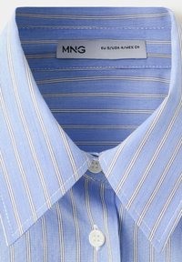 Chemise bleu clair avec fines rayures verticales blanches et foncées, boutons blancs et col, étiquetée MNG taille EU S USA 4 MEX CH.