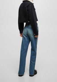 Veste en jean noire courte avec col en shearling, associée à un jean large taille haute à dégradé bleu et des bottes à plateforme noires.