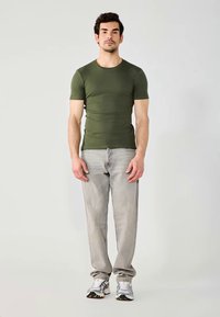 Tricou ajustat cu mânecă scurtă în verde măsliniu, asortat cu blugi gri deschis și adidași gri; design simplu cu o textură netedă.