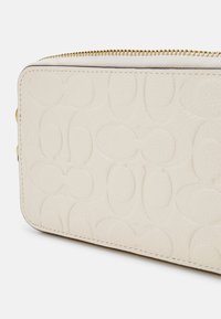 Kremowy portfel ze skóry z tłoczonym owalnym wzorem, złotym zamkiem błyskawicznym oraz gładką fakturą z przeszytymi krawędziami dla trwałości.