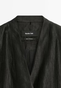 Schwarzer Leinenblazer mit V-Ausschnitt, der über eine glatte Textur und keine sichtbaren Verschlüsse verfügt. Das Etikett trägt "Massimo Dutti, Hergestellt in Portugal."