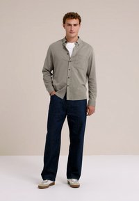 Lichtgrijs overhemd met knopen en een borstzak, gecombineerd met donkerblauwe wijde jeans en witte sneakers. Simpele, ontspannen pasvorm.