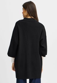 Black oversized sweater with a shawl collar, short sleeves, and a textured fabric, featuring a relaxed silhouette and soft drape.