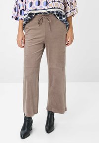 Bruine suède broek met wijde pijpen en een drawstring taille, met een gladde textuur, gecombineerd met zwarte enkellaarsjes. Geprint top gedeeltelijk zichtbaar.