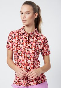 Short-sleeved shirt in red with a floral pattern featuring pink, purple, and black accents. Button-up design with a collar. Smooth texture.