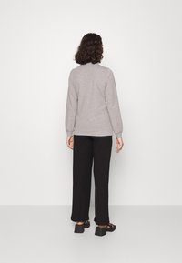 Sudadera gris con cuello redondo, puños y dobladillo acanalados, combinada con pantalones de pierna ancha negros y zapatos negros. Vista trasera del conjunto.