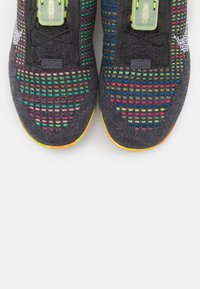 Graue Sportschuhe verfügen über ein strukturiertes Obermaterial mit mehrfarbigen Mustern. Grüne Hardwareakzente und eine leuchtende Sohle runden das Design ab.