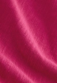 Gros plan sur un tissu froissé rose vif montrant un tissage texturé détaillé et des plis doux.