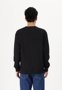 Sweatshirt noir à manches longues, col rond et poignets côtelés. Cintré à la taille, fabriqué en tissu doux, design minimaliste.