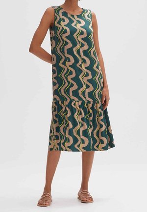 Vestido midi sin mangas con rayas onduladas en verde, beige y amarillo, cintura caída, acompañado de sandalias planas sobre fondo liso.