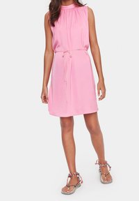 Vestido sin mangas de color rosa con escote fruncido y cintura con cordón, hecho de una tela suave. Combinado con sandalias planas que presentan un diseño de tiras trenzadas.