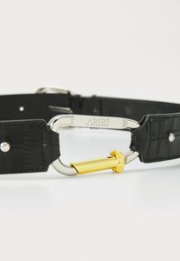 Curea din piele cu textura de crocodil, de culoare neagră, cu o cataramă argintie, care are gravat "ARIES" și un detaliu coloană auriu.