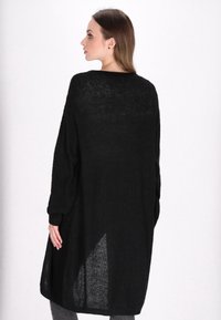Schwarzer gestrickter Cardigan mit lockerer Passform, langen Ärmeln und einer Lüftung auf der Rückseite. Texturierter Stoff und lässiges Design.
