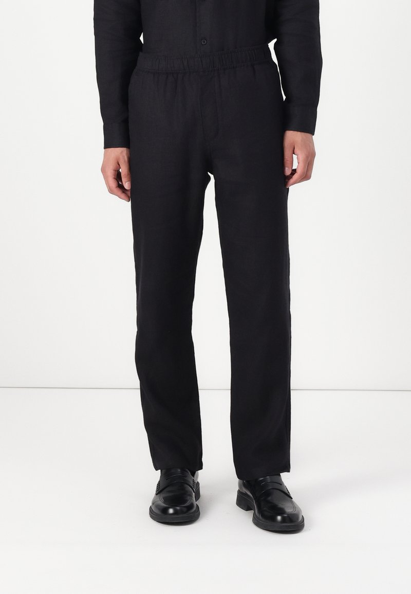 Black linen trousers with an elastic waistband, straight-leg design, and smooth texture. Paired with black shoes.