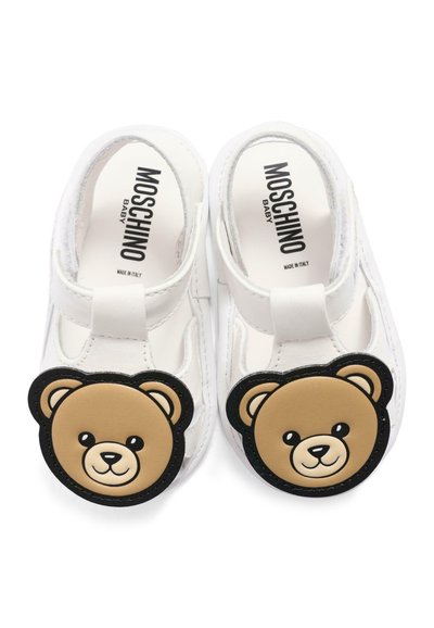Białe buty dziecięce z ozdobami w postaci buzi misia na przodzie oraz napisem "Moschino Baby" wewnątrz.
