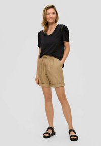 Czarny T-shirt z dekoltem w serek, z teksturowanymi bufkami, w połączeniu z jasnobrązowymi szortami z podwiniętymi nogawkami i czarnymi sandałami na platformie z plecionymi paskami.