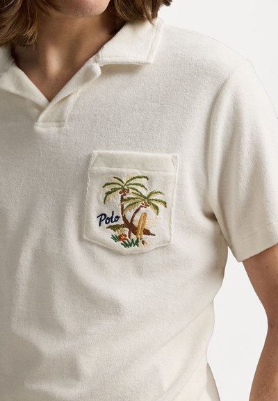 Bela bomba polo majica iz bombaža z teksturiranim finišem. Ima žep na prsih z barvitim vezenjem palme in surf deske.