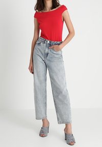Red off-shoulder top, high-waisted light blue denim jeans, and black-and-white striped open-toe heels. Casual, relaxed fit.