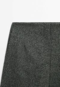 Gros plan de la partie supérieure d'un pantalon en tissu texturé gris foncé avec des coutures visibles le long de la ceinture.