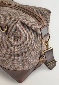 Woven fabric bag with multicolored texture; brown leather accents and a zip closure; adjustable strap with brass hardware.
