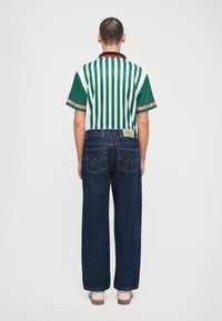 Green and white striped short-sleeve shirt with a black collar, paired with dark blue, wide-leg jeans, featuring a decorative back pocket design.