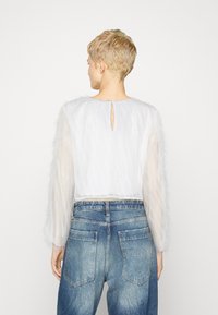 Vit kortärmad topp med genomskinliga, texturerade ärmar och detalj med nyckelhål bak, i kombination med högmidjade blå denimjeans.