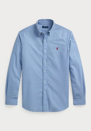 Chemise bleu clair à boutons, en coton, avec des manches longues, un col pointu et un petit logo rouge sur la poitrine gauche.