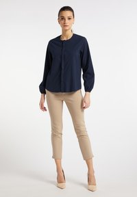 Mørkeblå langærmet skjorte med rund hals og knaplukning; parret med beige tætsiddende bukser og nude hæle.
