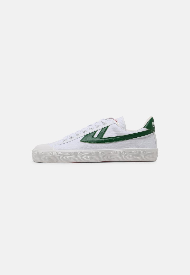 White canvas sneakers with green rubber accents, a textured white sole, and a low-top design featuring lace-up closure.