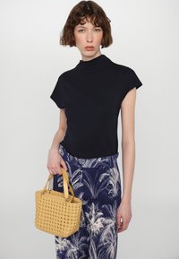 Navy short-sleeve top paired with high-waisted navy trousers featuring white palm leaf print; holding a small, woven yellow handbag.