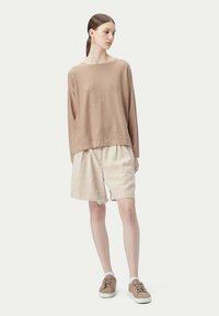 Beige långärmad stickad topp tillsammans med lösa krämfärgade shorts och tan sneakers. Har en avslappnad passform och minimalistic design.
