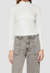 Weißes Langarmshirt mit Mock-Neck und dezentem Glanz, kombiniert mit grauen High-Waist-Jeans mit Fronttaschen und lockerer Passform.