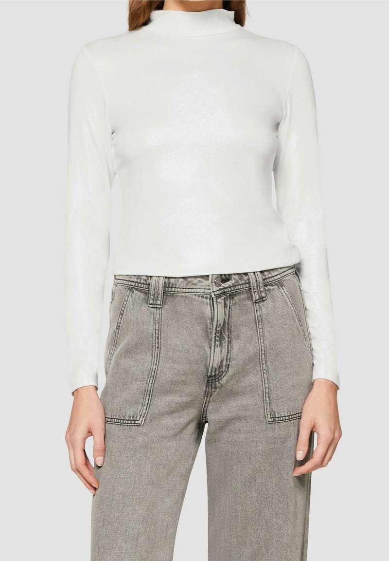 Weißes Langarmshirt mit Mock-Neck und dezentem Glanz, kombiniert mit grauen High-Waist-Jeans mit Fronttaschen und lockerer Passform.