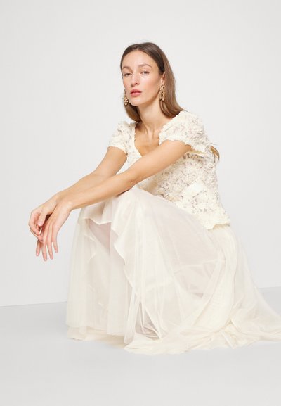 Top din dantelă florală ivorie cu mâneci scurte, asortat cu o fustă fluidă, din straturi, din material transparent, evidențiind un design și o textură ușoară, etereală.