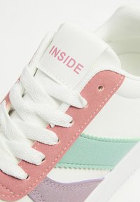 Zapatilla con parte superior de piel blanca y acentos de ante en color rosa, verde menta y lavanda. Texto "INSIDE" en la lengüeta. Cordones blancos.