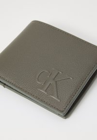Portafoglio in pelle grigia con finitura testurizzata, caratterizzato da un logo "CK" impresso. Design elegante con cuciture a contrasto e angoli arrotondati.