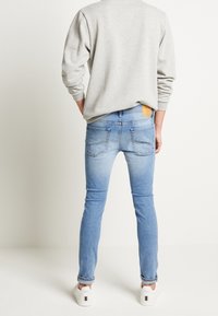 Ljusblå jeans med smal passform och en urblekt finish, bakfickor och en brun läderlapp på midjebandet. Matchat med en grå sweatshirt.