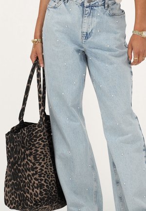 Jeans in denim chiaro con decorazioni in perle, abbinate a una borsa tote leopardata nera e beige con manici corti.