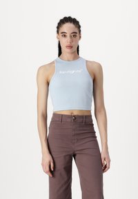 Top court en bleu clair à côtes avec un col rond et un logo brodé blanc. Associé à un pantalon texturé marron taille haute.