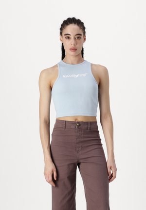 Lyseblå ribbet crop top med rund hals og hvit brodert logo. Kombinert med høy midje brune teksturerte bukser.