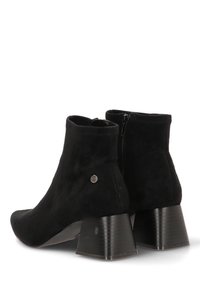 Botines de ante negro con tacón grueso, cremallera lateral y detalle metálico circular. Textura suave y diseño ajustado para soporte del tobillo.