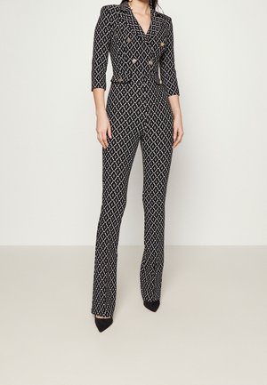 Schwarzer und weißer, gemusterter Jumpsuit mit Kragen, doppelter Knopfleiste auf der Vorderseite, taillierter Taille, Dreiviertelärmeln und ausgestellten Beinen.